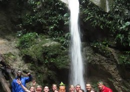 A group of travellers stand below a waterfall in the Amazon Jungle.
