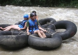 A group of three travellers rafting in the Amazon river on a raft made of inflated rubber rings.